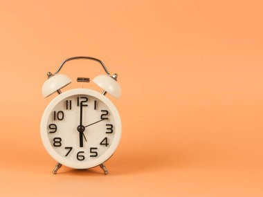 Beyaz antika alarmlı saatin ön görüntüsü saat 6 yönünde turuncu arka planda. Sabah rutini, günün yeni başlangıcı..