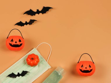 Cadılar Bayramı balkabağı, siyah kağıt yarasalar, tıbbi maske ve turuncu arka planda alkol dezenfektanı. Cadılar Bayramı, COVID-19 önleme ve yeni normal kavram.