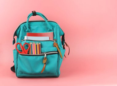 Okul malzemeleriyle dolu sırt çantasının önü. Pembe arka planda fotokopi alanı var. Okula ve eğitim konseptine dönüş.