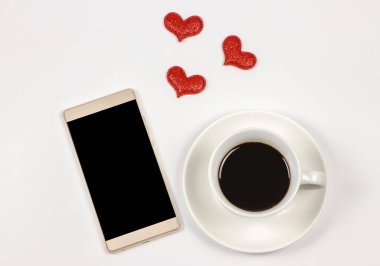 Üst ya da düz ekran cep telefonu, kahve fincanı ve beyaz arkaplan üzerinde kırmızı parıltılı kalpler. Sabah kahvesi, aşk, iletişim, online flört konsepti.