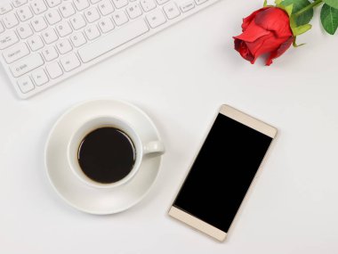 Üst ya da düz cep telefonu, kahve fincanı, bilgisayar klavyesi ve beyaz arka planda kırmızı gül. Pozitif sabah rutini, online randevu ve sevgililer günü konsepti..