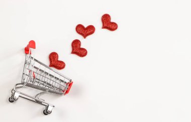 Beyaz arka plandaki alışveriş arabasından kopyalanmış kırmızı parıltılı kalplerin üst görüntüsü ya da düz yatağı. Sevgililer Günü, aşk alışverişi.