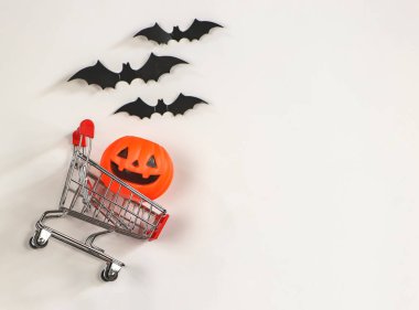 Cadılar Bayramı balkabağı alışveriş arabasında beyaz arka planda siyah kağıt yarasalar ve fotokopi alanı. Cadılar Bayramı konsepti.