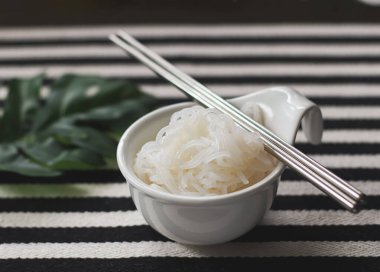 Konjac ya da Shirataki 'nin beyaz kasede metal çubuklar, siyah-beyaz çizgili masa örtüsü arka planı..