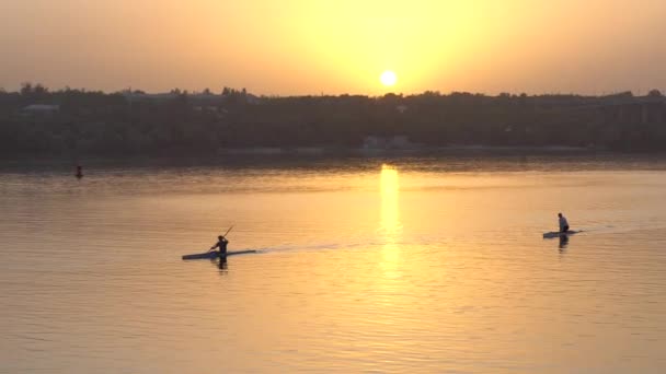 two guys kayak in the evening at sunset on the river water in which shimmers beautiful colors of yellow and orange shades