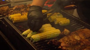 Büyük bir ızgarada, siyah eldivenli şefler büyük porsiyonlarda farklı et, domuz kebabı, sığır kebabı, tavuk, mısır kızartıyorlar, hızlıca maşayla sindiriyorlar.
