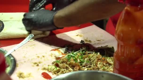 검은 장갑을 낀 맛있는 길거리 요리 요리사가 닭고기 고기와 신선 한 야채를 곁들인 피파 빵 샤르마를 싸고 있다 — 비디오