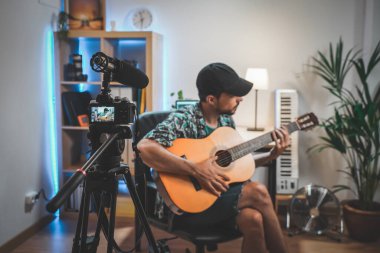 Gitar çalan genç bir adamın çekim sahnesinin arkasında. Çok yakışıklı ve sakallı bir adam sosyal medya için video çekiyor ve doğrudan kameraya konuşuyor. Etkilenenin çalışma alanı.