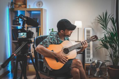 Gitar çalan genç bir adamın çekim sahnesinin arkasında. Çok yakışıklı ve sakallı bir adam sosyal medya için video çekiyor ve doğrudan kameraya konuşuyor. Etkilenenin çalışma alanı.