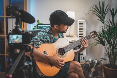 Gitar çalan genç bir adamın çekim sahnesinin arkasında. Çok yakışıklı ve sakallı bir adam sosyal medya için video çekiyor ve doğrudan kameraya konuşuyor. Etkilenenin çalışma alanı.