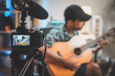 Gitar çalan genç bir adamın çekim sahnesinin arkasında. Çok yakışıklı ve sakallı bir adam sosyal medya için video çekiyor ve doğrudan kameraya konuşuyor. Etkilenenin çalışma alanı.