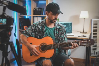 Gitar çalan genç bir adamın çekim sahnesinin arkasında. Çok yakışıklı ve sakallı bir adam sosyal medya için video çekiyor ve doğrudan kameraya konuşuyor. Etkilenenin çalışma alanı.