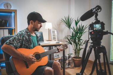 Gitar çalan genç bir adamın çekim sahnesinin arkasında. Çok yakışıklı ve sakallı bir adam sosyal medya için video çekiyor ve doğrudan kameraya konuşuyor. Etkilenenin çalışma alanı.