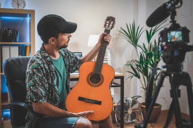 Gitar çalan genç bir adamın çekim sahnesinin arkasında. Çok yakışıklı ve sakallı bir adam sosyal medya için video çekiyor ve doğrudan kameraya konuşuyor. Etkilenenin çalışma alanı.