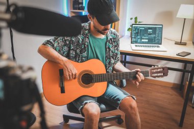 Gitar çalan genç bir adamın çekim sahnesinin arkasında. Çok yakışıklı ve sakallı bir adam sosyal medya için video çekiyor ve doğrudan kameraya konuşuyor. Etkilenenin çalışma alanı.