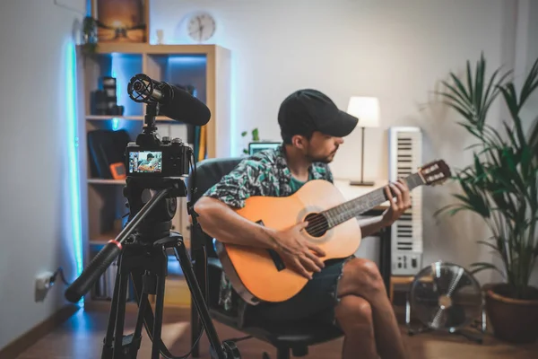 Gitar çalan genç bir adamın çekim sahnesinin arkasında. Çok yakışıklı ve sakallı bir adam sosyal medya için video çekiyor ve doğrudan kameraya konuşuyor. Etkilenenin çalışma alanı.