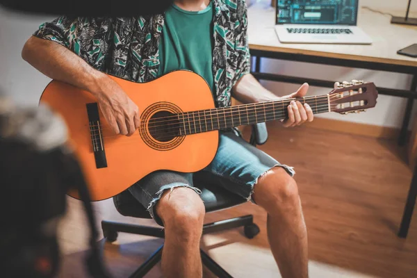 Behind the scene shot of a young man influencer making a video playing guitar. Very handsome man with beard shooting a video for social media talking directly to the camera. Influencer\'s work space.