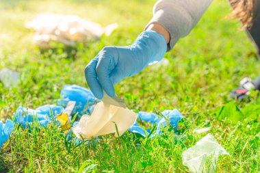 Coronavirus. Koronavirüs salgını sırasında yeşil çimenlerde uzanan mavi lastik eldivenler ve yüz maskeleri alan bir kadın. Çevre kirliliği. Kullanılmış. Çöp.. 