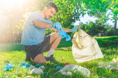 Coronavirus. Koronavirüs salgını sırasında yeşil çimlerin üzerinde duran mavi lastik eldivenler ve yüz maskeleri alan bir adam. Çevre kirliliği. Kullanılmış. Çöp.. 