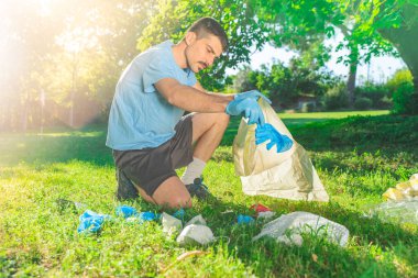 Coronavirus. Koronavirüs salgını sırasında yeşil çimlerin üzerinde duran mavi lastik eldivenler ve yüz maskeleri alan bir adam. Çevre kirliliği. Kullanılmış. Çöp.. 