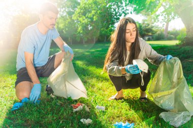 Coronavirus. Çift yeşil çimlerin üzerinde yatan koronavirüs salgını sırasında mavi lastik eldiven ve yüz maskesi alıyor. Çevre kirliliği. Çöp.. 
