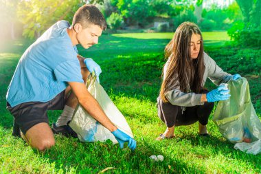 Coronavirus. Çift yeşil çimlerin üzerinde yatan koronavirüs salgını sırasında mavi lastik eldiven ve yüz maskesi alıyor. Çevre kirliliği. Çöp.. 