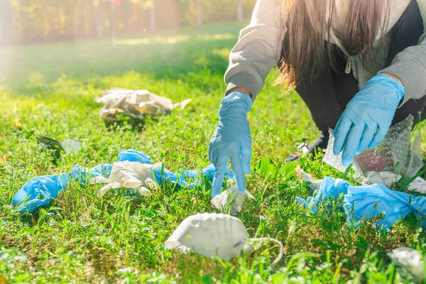 Coronavirus 在绿色的草地上 女人拿起蓝色的橡胶手套和面罩 环境污染 用过了垃圾 — 图库照片