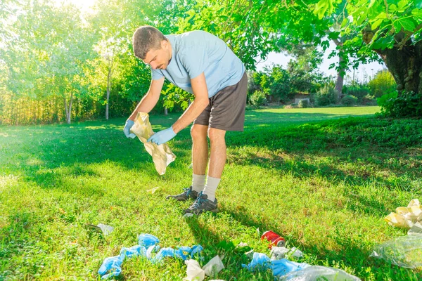 Coronavirus. Koronavirüs salgını sırasında yeşil çimlerin üzerinde duran mavi lastik eldivenler ve yüz maskeleri alan bir adam. Çevre kirliliği. Kullanılmış. Çöp.. 
