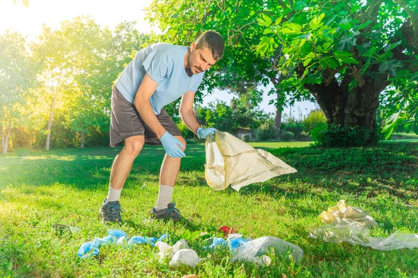 Coronavirus. Man picking up blue rubber gloves and face masks during coronavirus epidemic lying on green grass. Environment contamination. Used. Garbage.