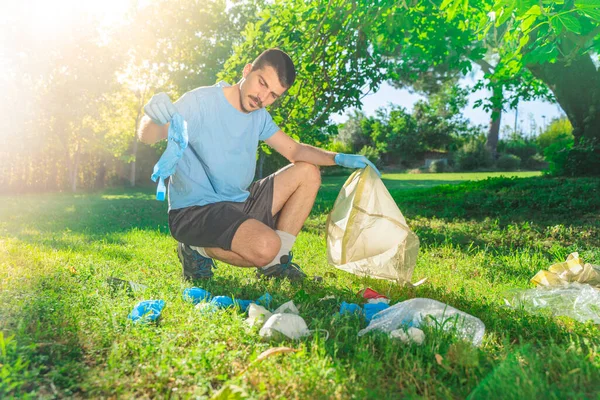 Coronavirus. Koronavirüs salgını sırasında yeşil çimlerin üzerinde duran mavi lastik eldivenler ve yüz maskeleri alan bir adam. Çevre kirliliği. Kullanılmış. Çöp.. 