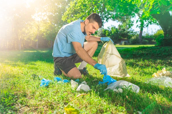 Coronavirus. Koronavirüs salgını sırasında yeşil çimlerin üzerinde duran mavi lastik eldivenler ve yüz maskeleri alan bir adam. Çevre kirliliği. Kullanılmış. Çöp.. 
