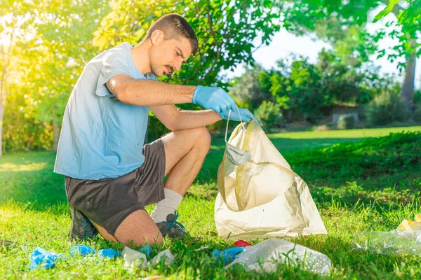 Coronavirus. Koronavirüs salgını sırasında yeşil çimlerin üzerinde duran mavi lastik eldivenler ve yüz maskeleri alan bir adam. Çevre kirliliği. Kullanılmış. Çöp.. 