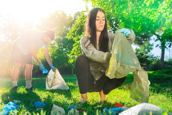 Coronavirus. Couple picking up blue rubber gloves and face masks during coronavirus epidemic lying on green grass. Environment contamination. Garbage.