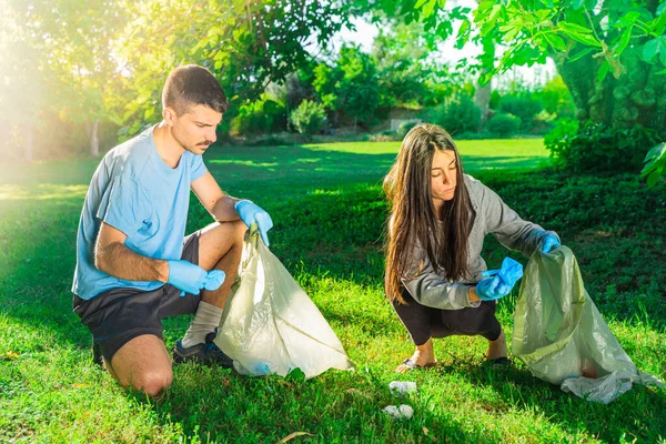 Coronavirus. Couple picking up blue rubber gloves and face masks during coronavirus epidemic lying on green grass. Environment contamination. Garbage.
