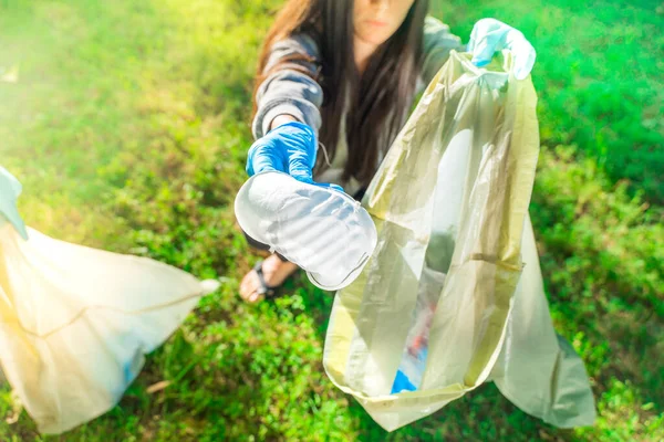 Coronavirus. Woman picking up blue rubber gloves and face masks on green grass during coronavirus epidemic. Environment contamination.  Garbage.