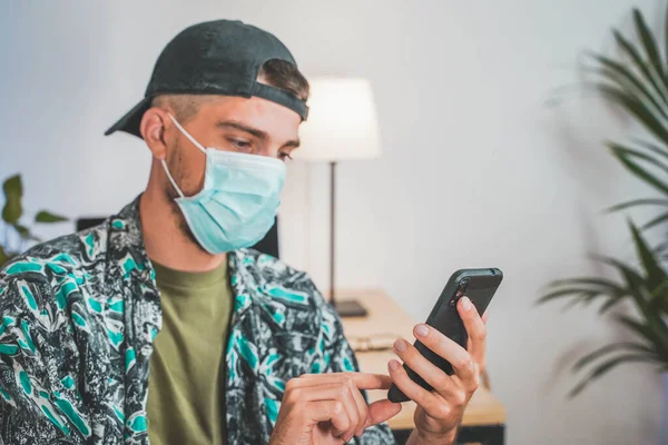 Young man with face mask working from home with mobile phone. Influencer setting up to make a online video. Amazing work space. Working in video and photo edit.