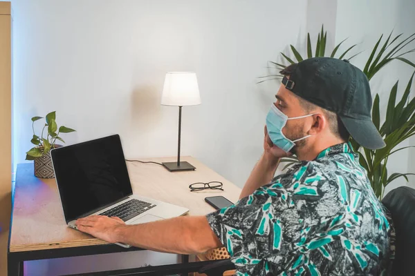 Young man with face mask working from home with laptop. Influencer setting up to make a online video. Amazing work space. Working in video and photo edit. Coronavirus.