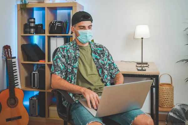 Young man with face mask working from home with laptop. Influencer setting up to make a online video. Amazing work space. Working in video and photo edit. Coronavirus.