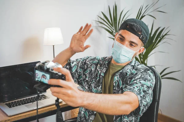Young man with face mask working from home with video camera. Influencer setting up to make a online video. Amazing work space. Working in video and photo edit. Coronavirus.