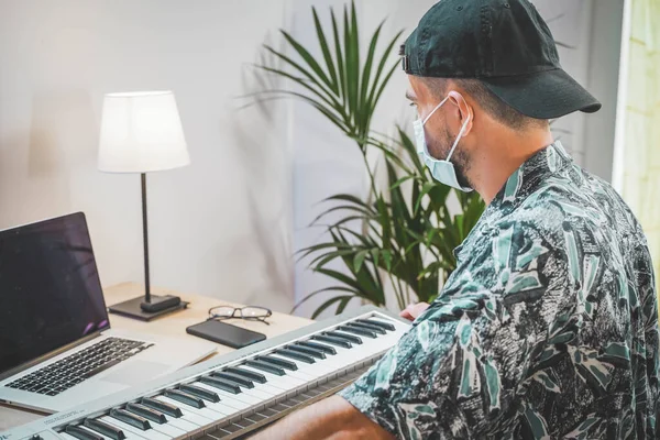Young man with face mask working from home. Songwriting and music producer. Amazing work space. Working in video and photo edit. Playing piano.