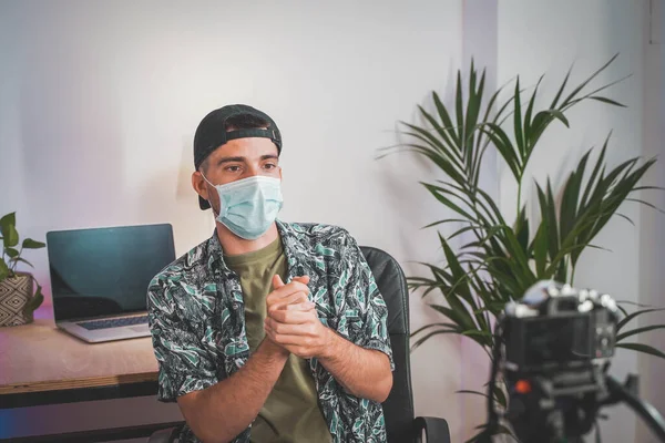 Young man with face mask working from home with video camera. Influencer making online video. Amazing work space. Working in video and photo edit.
