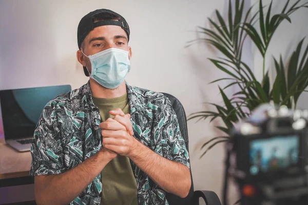 Young man with face mask working from home with video camera. Influencer making online video. Amazing work space. Working in video and photo edit.