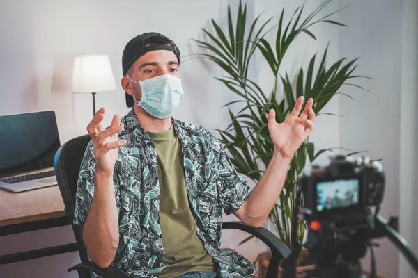 Young man with face mask working from home with video camera. Influencer making online video. Amazing work space. Working in video and photo edit.
