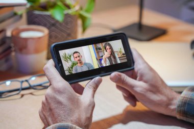 Bir iş adamının iş arkadaşlarıyla video konferans planı hakkında konuştuğu görüntüler. İş ekibi görüntülü görüşme için cep telefonunu kullanıyor. Evden çalışan bir grup zeki insan..