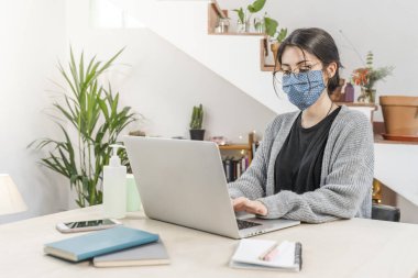 Coronavirus. Genç bir iş kadını koruyucu maske takarak evden izole edilmiş. Coronavirus yüzünden karantinada olan kadın maske takıyor. Dezenfektan jeliyle evden çalışıyor. Karantina. 