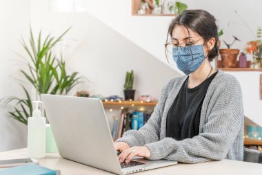 Coronavirus. Genç bir iş kadını koruyucu maske takarak evden izole edilmiş. Coronavirus yüzünden karantinada olan kadın maske takıyor. Dezenfektan jeliyle evden çalışıyor. Karantina. 