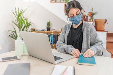 Coronavirus. Genç bir iş kadını koruyucu maske takarak evden izole edilmiş. Coronavirus yüzünden karantinada olan kadın maske takıyor. Dezenfektan jeliyle evden çalışıyor. Karantina. 