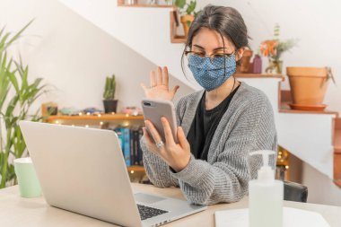 Coronavirus. Genç bir iş kadını koruyucu maske takarak evden izole edilmiş. Coronavirus yüzünden karantinada olan kadın maske takıyor. Cep telefonuyla çalışıyorum. Karantina. 