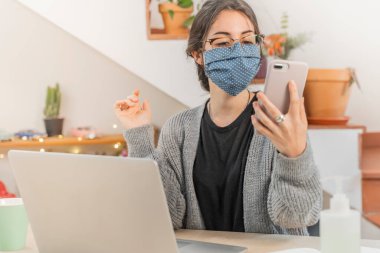 Coronavirus. Genç bir iş kadını koruyucu maske takarak evden izole edilmiş. Coronavirus yüzünden karantinada olan kadın maske takıyor. Cep telefonuyla çalışıyorum. Karantina. 