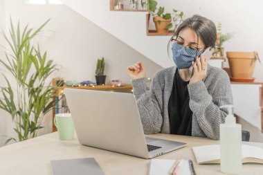 Coronavirus. Genç bir iş kadını koruyucu maske takarak evden izole edilmiş. Coronavirus yüzünden karantinada olan kadın maske takıyor. Cep telefonuyla çalışıyorum. Karantina. 